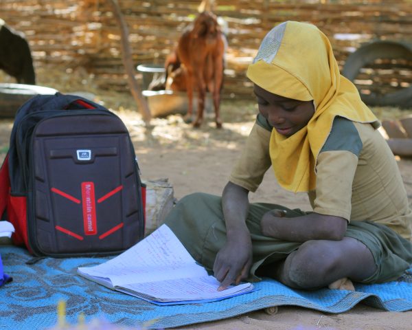 Pige læser i sin skolebog udendørs.