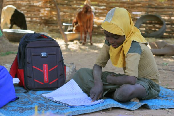 Pige læser i sin skolebog udendørs.