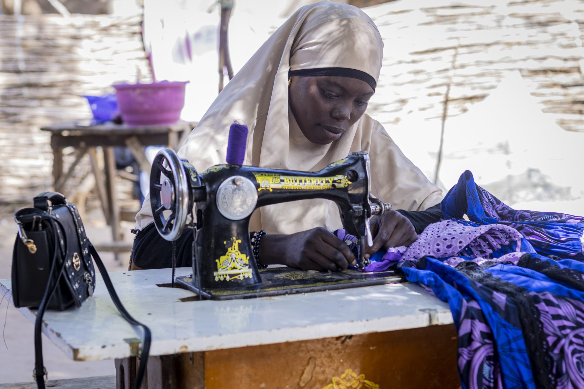 Zahara Seybou Harouna arbejder koncentreret udenfor ved sin symaskine. Niger 2023