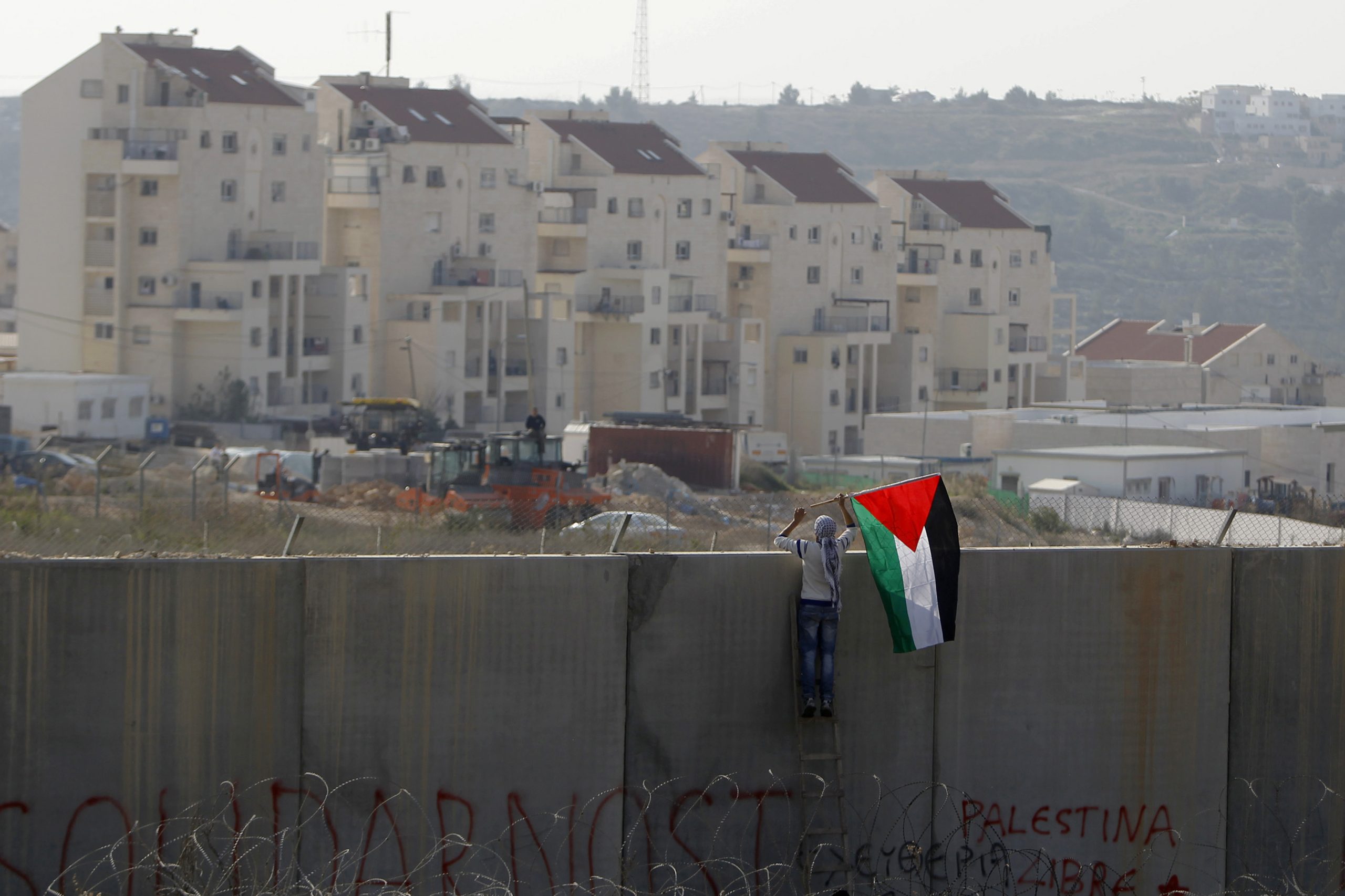 A Palestinian protester places a flag on the controversial Israeli barrier during clashes with Israeli security officers near Ramallah