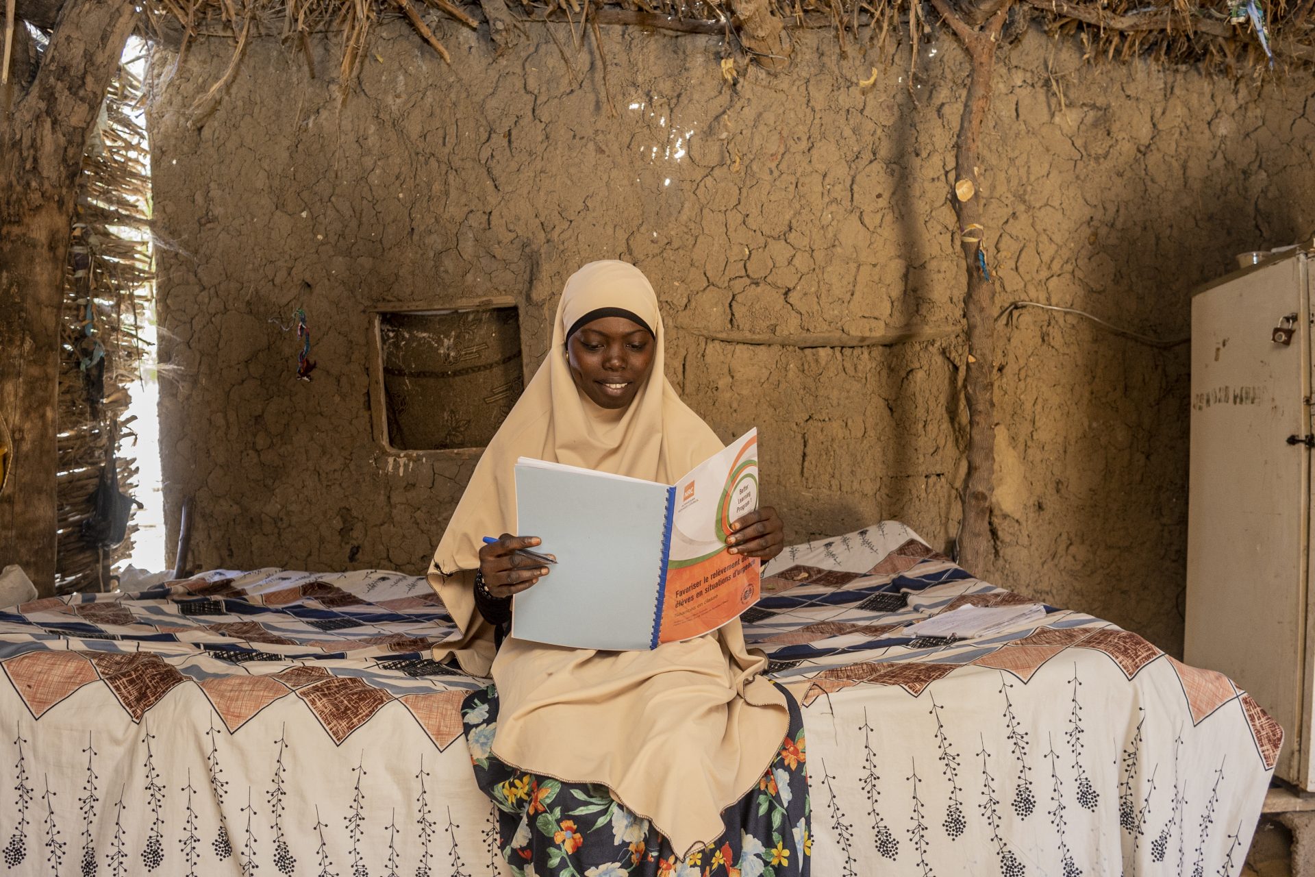 Zahara Seybou Harouna, Niger, sidder på sengen i sit hjem med en bog i hænderne og læser.
