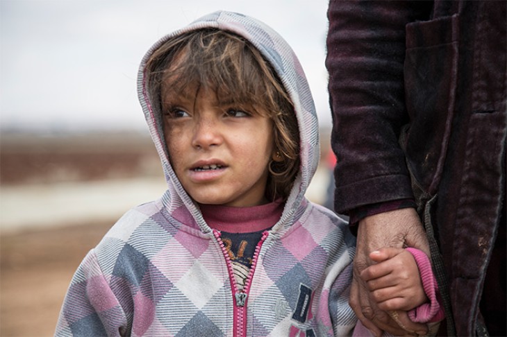Syrisk flygtningebarn holder en voksen i hånden.