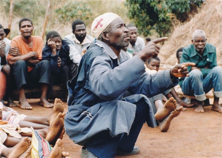 Mand sidder på hug foran folkemængde