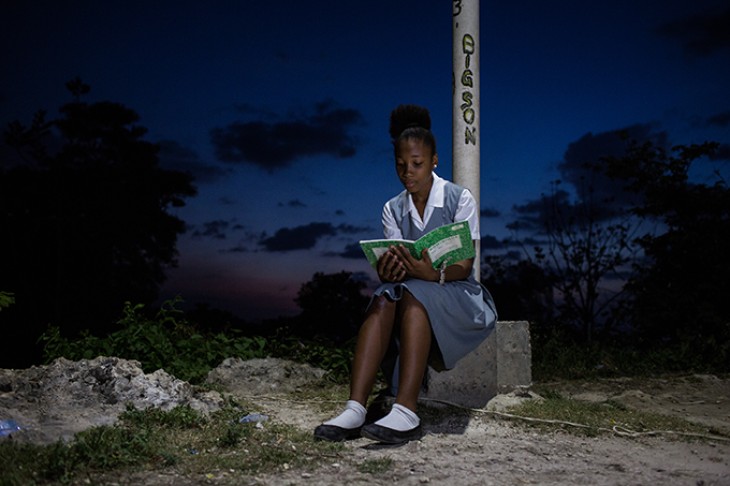 Pige læser i skolebog i lyset fra solcellelampe - Haiti