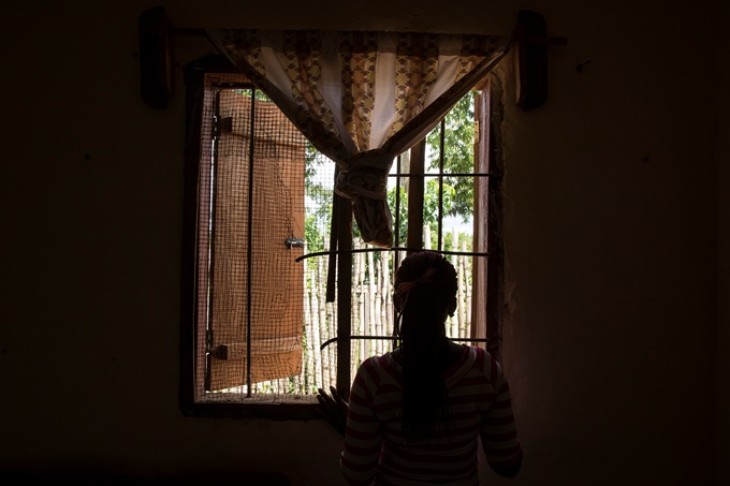 Kvinde foran vindue i mørkt rum.