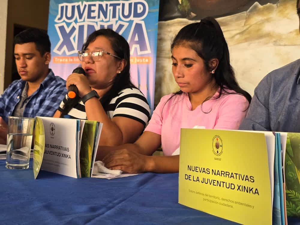 to kvinder der sidder ved et bord hvor den ene taler i en mikrofon